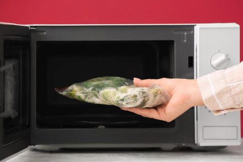 Lady putting vegetable for thawing in microwave